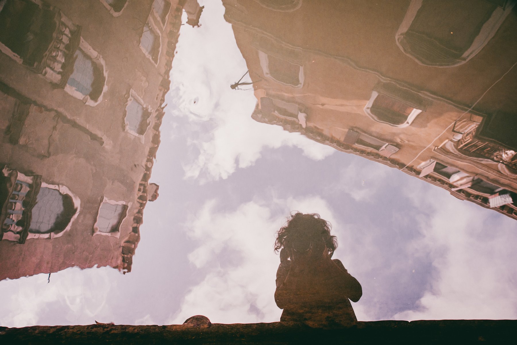 A self-portrait reflected in a puddle on cobbled streets